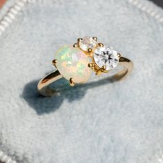 an opal and diamond ring sitting on top of a cloth