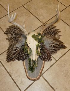 an animal skull with antlers and foliage on it's head sitting on a tile floor