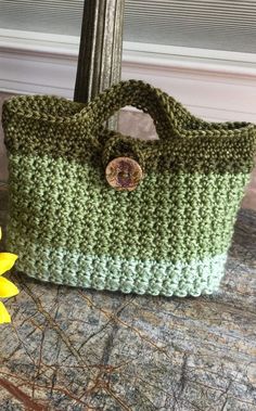 a green crocheted purse sitting on top of a table next to a yellow flower