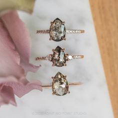 three rings with different colored stones on them next to a pink flower and white background