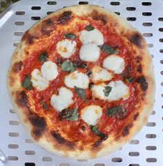 a pizza with mozzarella and basil on it sitting on a cooling rack in the sun