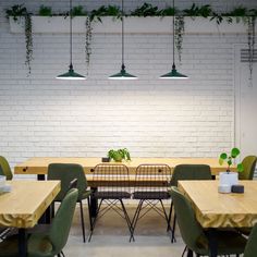 an empty restaurant with green chairs and wooden tables in front of a white brick wall