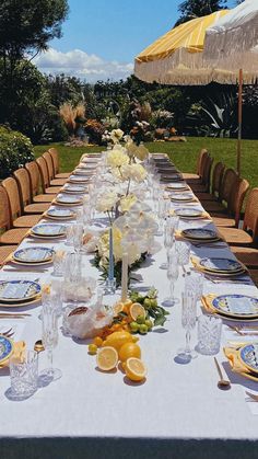 a long table set with plates, glasses and lemons on it in front of an umbrella