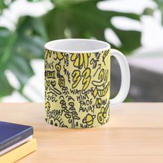 a yellow and black coffee mug sitting on top of a wooden table next to a book