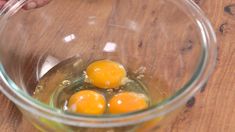 three eggs in a glass bowl on top of a wooden table next to a person's hand