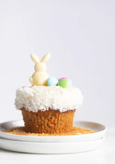 a cupcake with white frosting and some candy eggs in it on a plate