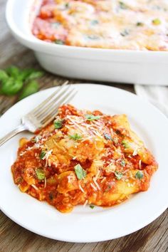 a white plate topped with lasagna next to a casserole dish on a wooden table