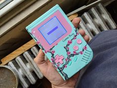 a person holding a game boy case in their left hand, with pink and blue flowers on it