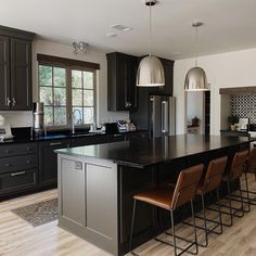 a large kitchen with black cabinets and an island in the middle is shown, along with bar stools