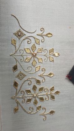 an embroidered piece with gold and silver designs on white fabric, next to a needle