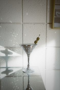 a martini glass with two olives in it sitting on a counter next to a white tiled wall