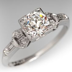 This lovely architectural circa 1920s Art Deco ring is centered with one (1) old European cut diamond, weighing 0.95 carats, that is prong set in a square frame with milgrain edging. Each shoulder is accented with three (3) bead set round single cut diamonds, and one (1) bezel set baguette cut diamond. The shoulders also have milgrain edges. The ring measures 6.2mm at the top, rises 6.1mm above the finger, tapering to 1.3mm wide and 1.0mm thick at the base of the shank.  The ring is crafted in platinum and is currently a size 5.  One of the baguette diamonds has a tiny corner chip that cannot be seen while worn. Luxury Single Diamond Art Deco Ring, Luxury Art Deco Diamond Ring With Prong Setting, Luxury Diamond White Sapphire Art Deco Ring, Luxury Art Deco Ring With Polished Finish, Luxury Art Deco Princess Cut Diamond Ring, 1920 Engagement Ring Diamond, Luxury Art Deco White Sapphire Ring, Luxury Art Deco Diamond Ring With Polished Finish, Luxury Art Deco Diamond Ring With Single Diamond