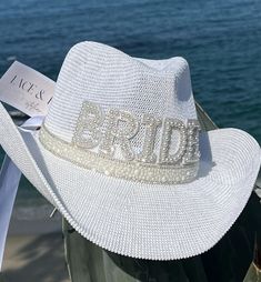 a white hat with the word bride written on it sitting next to some clothes and water