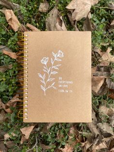 a notebook with the words do everything in love written on it sitting among leaves and grass