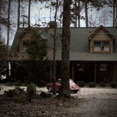 a car is parked in front of a log cabin with trees and rocks on the ground