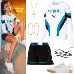 a woman in white shirt and black shorts sitting next to a pair of shoes with puma on it