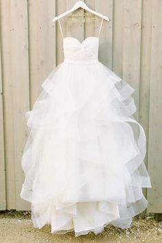 a wedding dress hanging on a hanger in front of a wooden wall with white paint