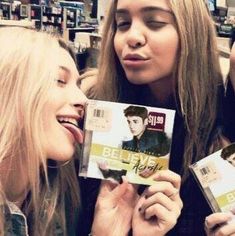 three young women are holding up cds in a store, one is smiling and the other has her mouth open