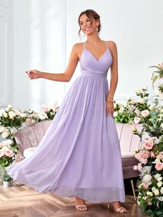 a woman in a long purple dress standing on a wooden floor with flowers behind her