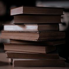 a stack of brown books sitting on top of a wooden table next to a cup