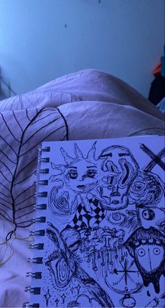 an open notebook sitting on top of a bed next to a lamp and a drawing