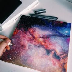 a person is drawing on a piece of paper that has been painted with watercolors