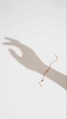 the shadow of a person's hand on a white wall with a gold chain