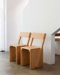 two wooden chairs sitting next to each other in front of a white wall and stairs