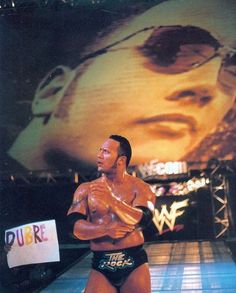 a man standing on top of a wrestling ring in front of a large screen with the image of wrestler john cena