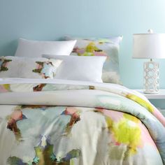 a bed with colorful comforters and pillows on it next to a night stand in front of a blue wall