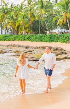 an older couple holding hands while walking on the beach with palm trees in the background