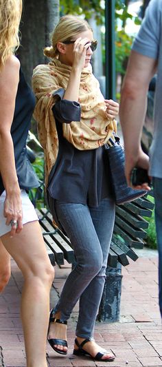 a woman talking on a cell phone while standing next to a park bench with people