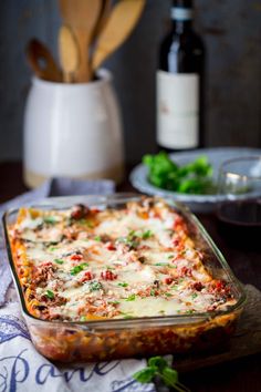 a casserole dish with meat, cheese and vegetables in it next to a bottle of wine