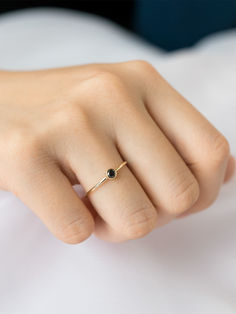 a woman's hand wearing a gold ring with a black diamond on it, resting on a white sheet