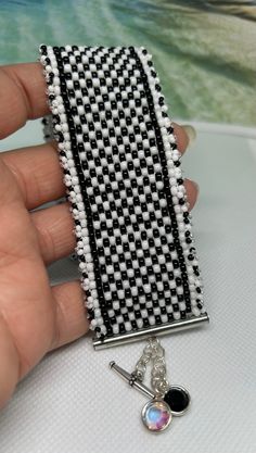 a hand holding a black and white beaded brooch on a table next to a piece of jewelry