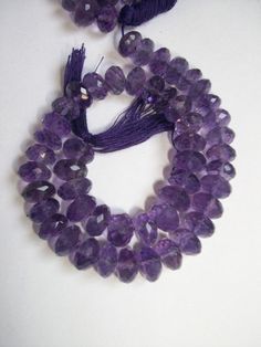 two strands of amethyst beads with tassels on a white table top