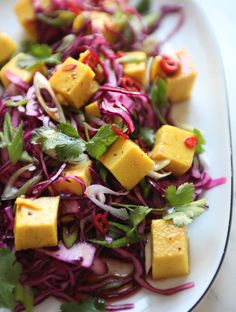 a white plate topped with salad and tofu on top of red cabbage slaw