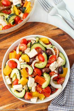 a salad with cucumbers, tomatoes, olives and feta cheese in a white bowl