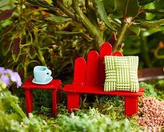 a small red bench sitting in the middle of a garden filled with plants and flowers