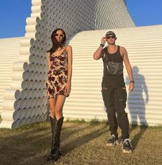 two people standing next to each other in front of a building with pipes on it