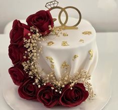 a wedding cake decorated with red roses and gold leaves on a white platter,