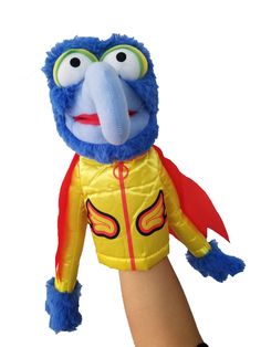 a hand holding a blue and yellow stuffed animal with an orange jacket on it's chest