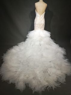 a white wedding dress with feathers on the bottom and back, in front of a mannequin