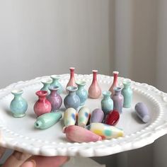 a person holding a white plate with many small ceramic vases on top of it