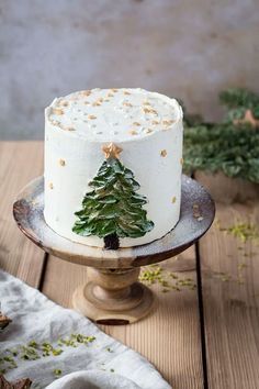 a white cake decorated with a green christmas tree on a wooden table next to other holiday decorations