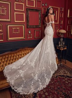 a woman in a white wedding dress standing next to a couch with red walls behind her