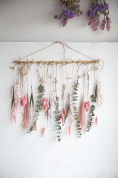 flowers hanging from a rope on a white wall next to purple and pink flowers in vases