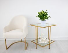 a white chair next to a glass table with a potted plant on it and a gold frame