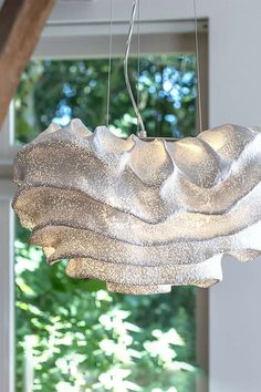 a light fixture hanging from a ceiling in front of a window with trees behind it