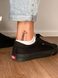 a giraffe tattoo on the ankle of a woman's foot, next to a pair of black tennis shoes